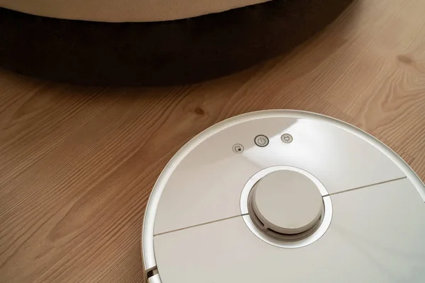 robot vacuum cleaner removes dust in room on brown floor. vacuum cleaner in ordinary apartment. modern household wireless device for cleaning house. smart home concept