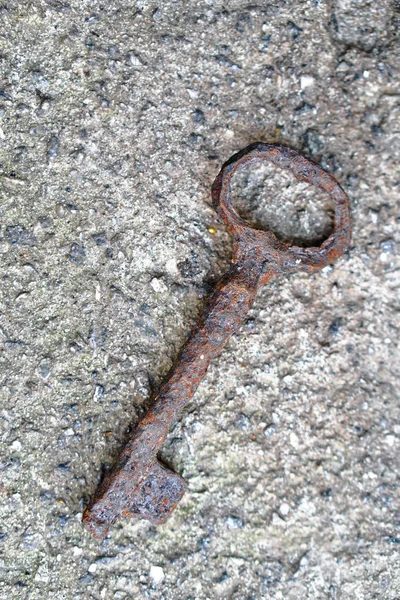 An antique rusty metal key on the background of concrete. A romantic secret protected by mystery. Stock photo.