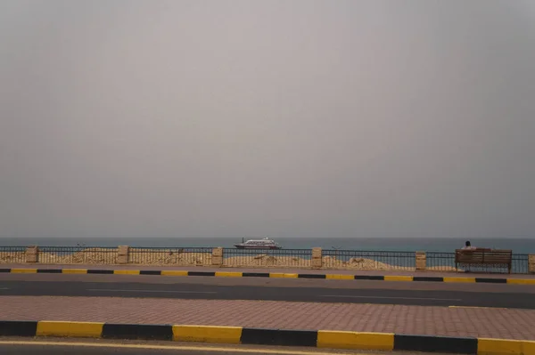 海の背景に対して アスファルト道路海 ベンチに孤独な男 デザインのストック フォト — ストック写真