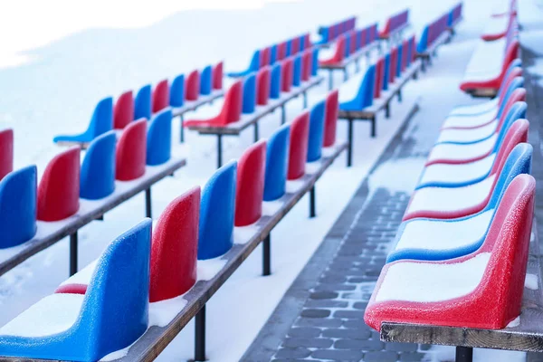 Snow-covered multi-colored seats in the stadium in winter. Snowfall interferes with sports. Uncleaned stadium. ecological disaster freeze — ストック写真