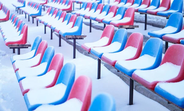 Snow-covered multi-colored seats in the stadium in winter. Snowfall interferes with sports. Uncleaned stadium. ecological disaster freeze — ストック写真