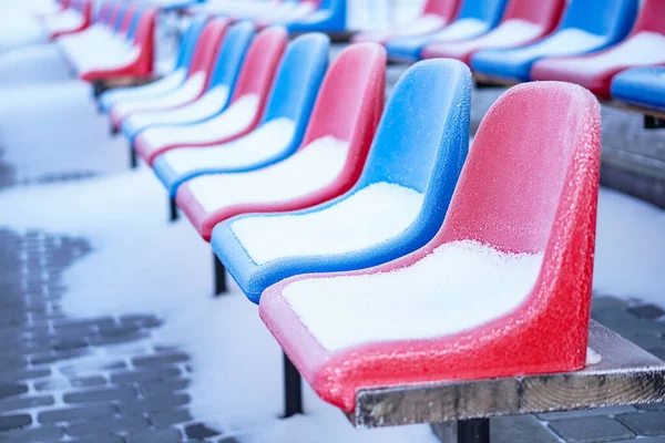 Snow-covered multi-colored seats in the stadium in winter. Snowfall interferes with sports. Uncleaned stadium. ecological disaster freeze — ストック写真