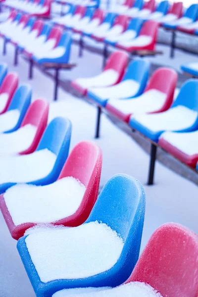 Snow-covered multi-colored seats in the stadium in winter. Snowfall interferes with sports. Uncleaned stadium. ecological disaster freeze — ストック写真