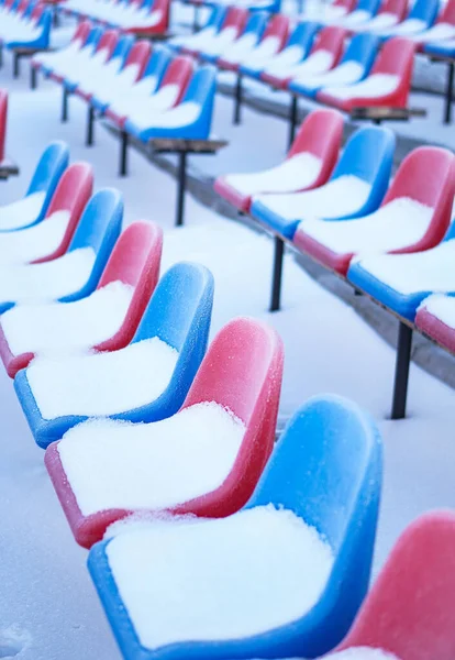 Snow-covered multi-colored seats in the stadium in winter. Snowfall interferes with sports. Uncleaned stadium. ecological disaster freeze — ストック写真