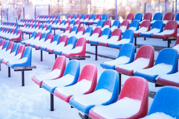 Snow-covered multi-colored seats in the stadium in winter. Snowfall interferes with sports. Uncleaned stadium. ecological disaster freeze — ストック写真