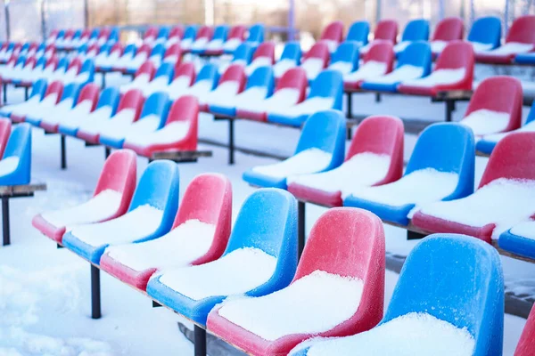 Snow-covered multi-colored seats in the stadium in winter. Snowfall interferes with sports. Uncleaned stadium. ecological disaster freeze — ストック写真