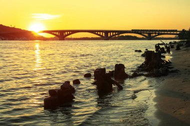 Gün batımında bir nehirde ya da gölde şehrin arka planına ve köprüye doğru sürükleniyor. Suyla ve eski kütüklerle manzara. Tasarım için stok fotoğrafı