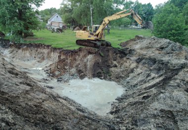 Bir kazıcı ev inşa etmek için büyük bir çukur kazar. Bir traktör zaten su kazanan büyük bir göl kazıyor. Tasarım için stok arkaplanı