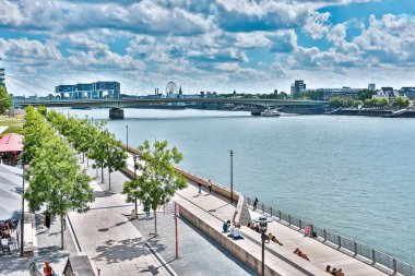 Köln, Almanya - 27 Haziran 2020: Güneşli bir günde vinç evleri ve dönme dolabı olan Skyline Köln. Ren Nehri 'nin kıyısındaki insanlar .