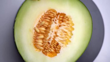 Tohumlarla dolu yarım bir kavun dönüyor, taze dokuyu ve tropikal meyvelerin doğal detaylarını gösteriyor. Sahnede tazelik, beslenme ve sağlıklı gıda kavramları vurgulanıyor.