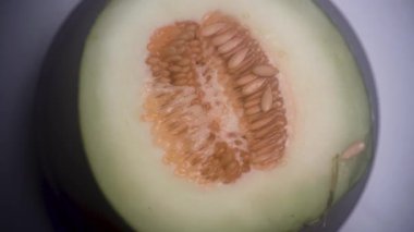 Çekirdekle dolu yarım parça kavun dönüyor, nötr renk derecelendirme ile üst açıdan çekiliyor. Çekim, taze dokuyu ve meyvenin doğal detaylarını vurguluyor. 4K görüntü