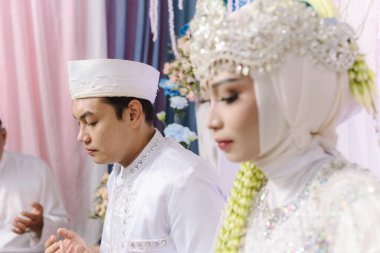 Yeni evli bir koca, nikahtan sonra karısının yanında dua etmek için ellerini kaldırır. Huzurlu ve anlamlı bir manevi an yakalar. Duruşları minnettarlığı, inancı ve birliği yansıtıyor.