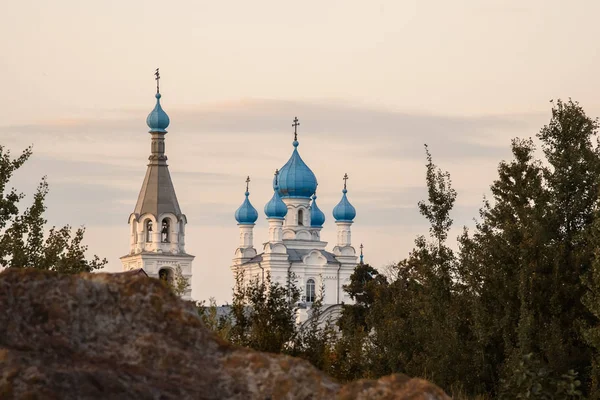 Vit-sten kyrkan med blå kupoler akgrunden rock mot kvällshimlen. — Stockfoto