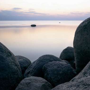 Turuncu günbatımı tonted denizde arka plan üzerinde büyük taşlar.