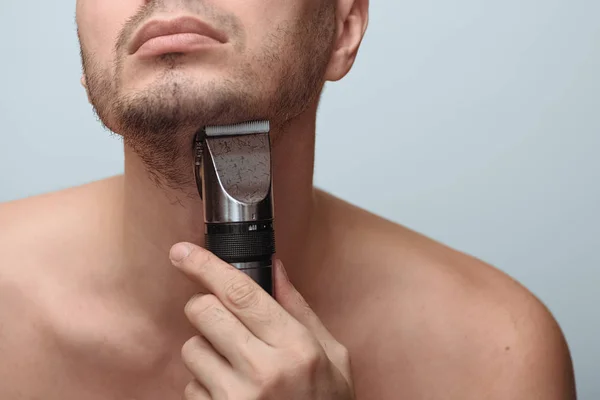 Imagem recortada de um jovem barbudo usando barbeador elétrico isolado sobre fundo cinza — Fotografia de Stock