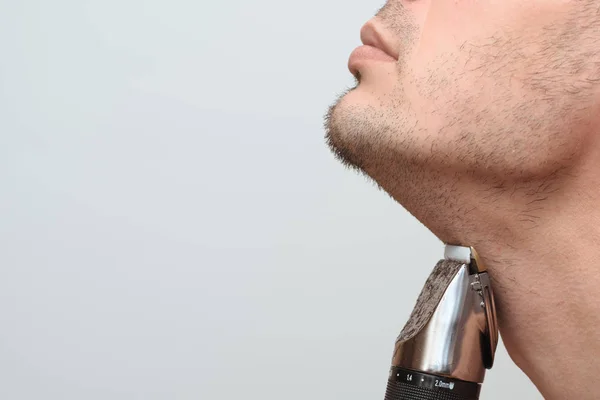 裁剪图像侧视图的一个年轻的胡须男子使用电动剃须刀隔离在灰色背景。带有复制空间的照片. — 图库照片