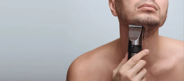 Imagen recortada de un joven barbudo usando afeitadora eléctrica aislada sobre fondo gris —  Fotos de Stock