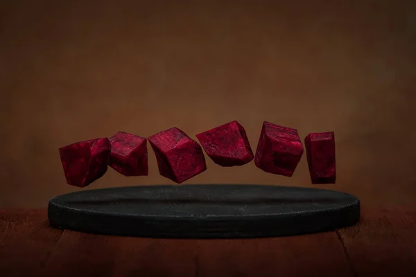 Levitazione vegetale. Cubi di barbabietola in aria su uno sfondo di legno marrone . — Foto Stock