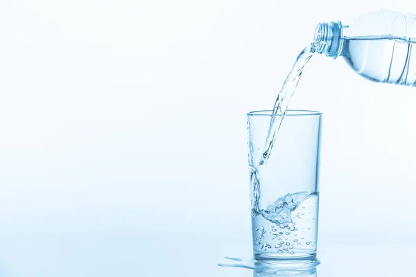 Menuangkan air dari botol ke gelas dengan latar belakang biru. Foto dengan ruang fotokopi . — Stok Foto