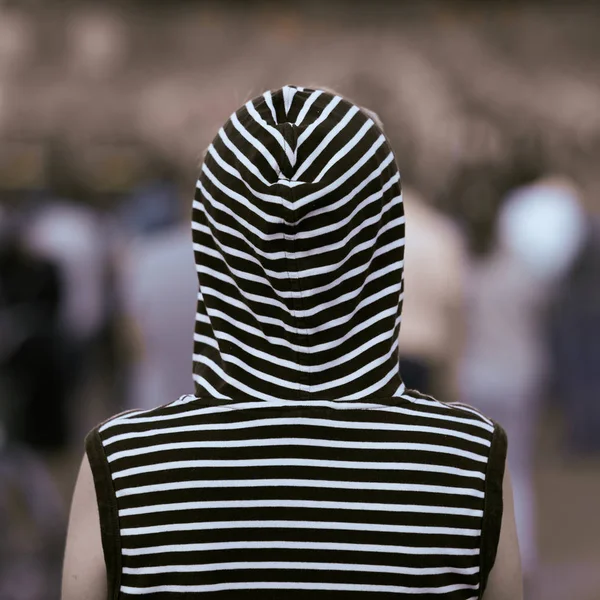 Vue arrière fille solitaire dans un gilet avec une capuche se tient à un concert de rue. Contexte en flou . — Photo