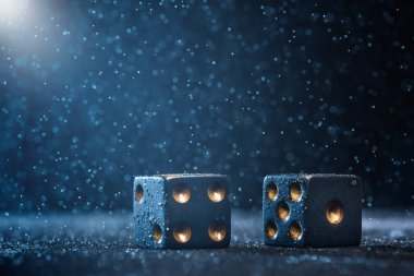 Mavi arka plan üzerinde parlak ışıkla aydınlatılan iki siyah zar. Kumar kavramı.