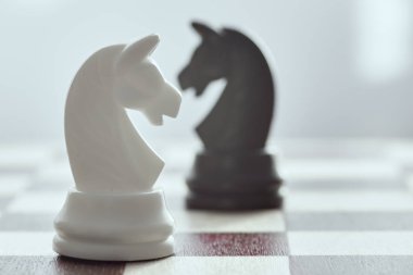 Beyaz satranç atı bulanık bir şekilde siyah bir atın üzerine yakın. Yüzleşme kavramı. Satranç bir strateji ve zeka kurulu oyunudur.