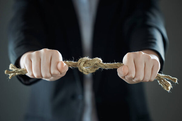 Horizontal shot of businessman's hands tighten the rope knot against background of suit in blur. People and business concept.