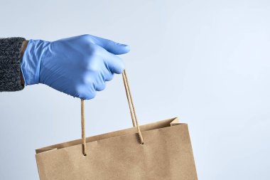 Mavi lastik eldivenler kağıt bir torba tutuyor. Güvenli alışveriş konsepti. Koronavirüs salgınının karantinası sırasında yiyecek teslimatı..