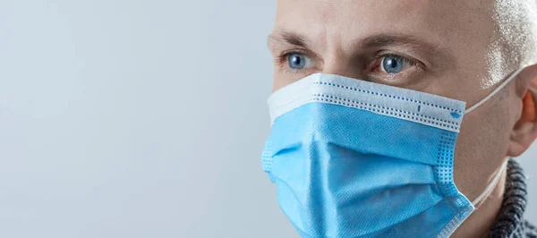 Horizontal shot of man in a medical mask close-up on a gray background.