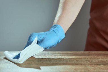 Tıbbi eldivendeki yatay el resmi masayı peçeteyle siler. Bulanık önlüklü arka plan garsonu. Yüzey tedavisi.