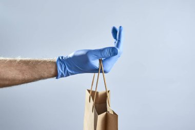 Mavi kauçuk eldivenli yatay bir el resmi gri arka planda bir kese kağıdı tutuyor..