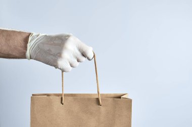 Beyaz kauçuk eldivenli yatay el resmi gri arka planda bir kese kağıdı tutuyor. Fotoğraf alanı kopyala.