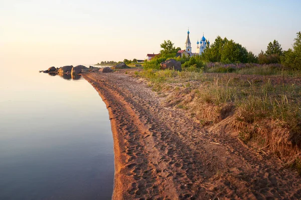La orilla del lago Peipus al atardecer. Iglesia de los apóstoles Pedro y Pablo en Vetvenik, región de Pskov. — Foto de Stock