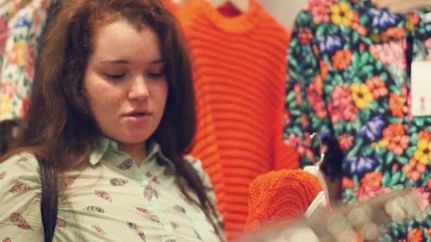 Молодая женщина в магазине выбирает теплую зимнюю одежду — стоковое видео