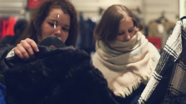 Dos mujeres jóvenes compran en la tienda eligiendo ropa de invierno caliente — Vídeos de Stock