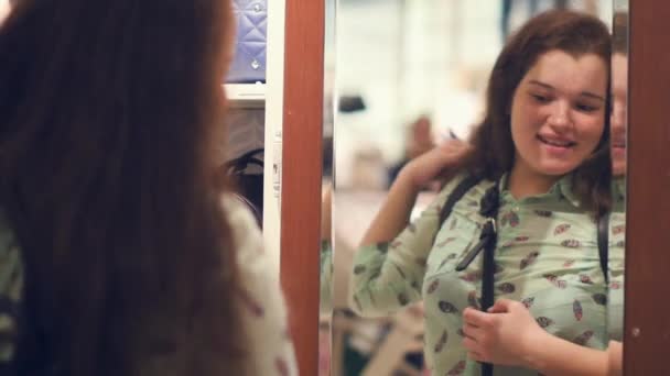 Una mujer joven en una tienda está eligiendo una bolsa, de pie junto al espejo en la tienda — Vídeo de stock