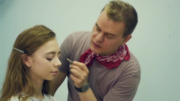 En manlig make-up artist sätter på make-up en ung kvinna. Befälhavaren berättar om makeup för en grupp flickor. Mästarklass för make-up artister. — Stockvideo