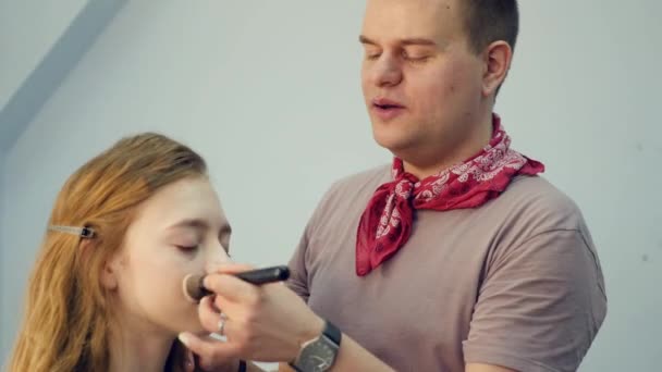 Um maquiador masculino põe maquilhagem numa jovem. O mestre conta sobre a maquilagem de um grupo de meninas. Master class para maquiadores . — Vídeo de Stock
