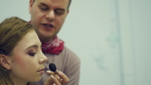 Un maquillador masculino maquilla a una joven. El maestro cuenta sobre el maquillaje para un grupo de chicas. Master class para maquilladores . — Vídeos de Stock