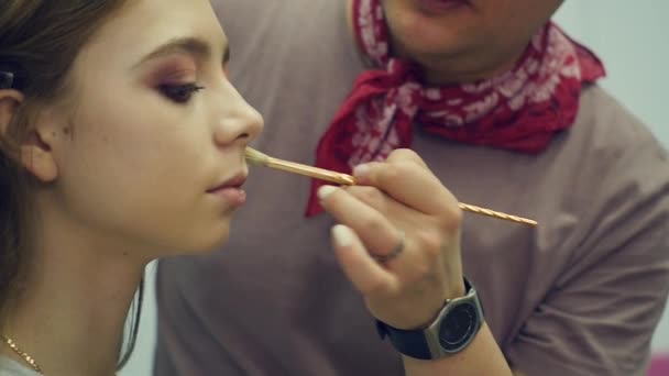 Mężczyzna make-up artist stawia na makijaż młoda kobieta. Kapitan opowiada o makijażu dla grupy dziewcząt. Klasy mistrzowskiej dla wizażystów. — Wideo stockowe