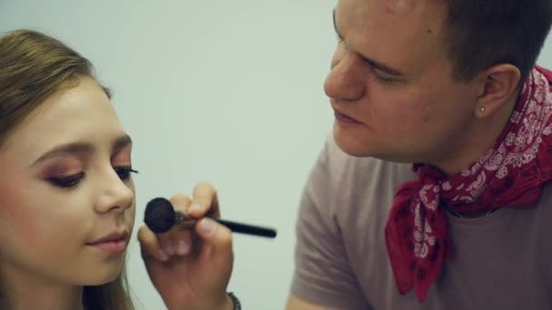 Un maquillador masculino maquilla a una joven. El maestro cuenta sobre el maquillaje para un grupo de chicas. Master class para maquilladores . — Vídeos de Stock