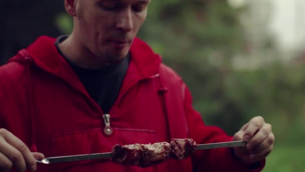 Een man eet gebakken vlees in de open lucht — Stockvideo