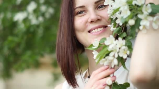 Beautiful girl portrait near a flowering tree in the park. The concept of youth and natural beauty. A young girl smells like the apple tree in the spring in the garden — Stock Video