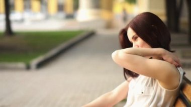 Güzel genç kadın gizemli bir şekilde, bir yaz parkta bir bankta oturan gülümsüyor. Açık havada bir kadın portresi.