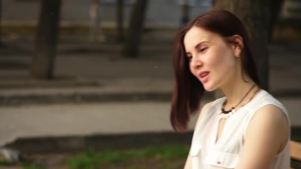 Όμορφη Νεαρή Γυναίκα Χαμόγελα Μυστηριωδώς Κάθεται Ένα Παγκάκι Στο Πάρκο — Αρχείο Βίντεο