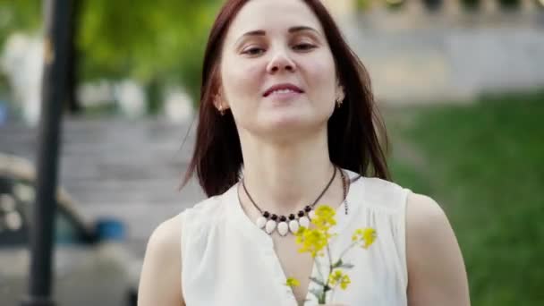 Retrato de una mujer sonriente al aire libre. Flores amarillas en las manos de las mujeres — Vídeos de Stock