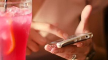 Bir akıllı telefon elinde güzel bir kadınla bir kokteyl barda içecekler.