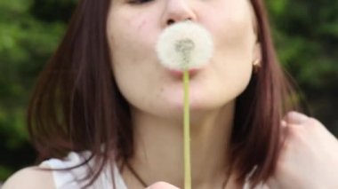 Genç bir sevimli kadın karahindiba karşı bir yaz yeşil bahçe zemin üzerinde üfleme