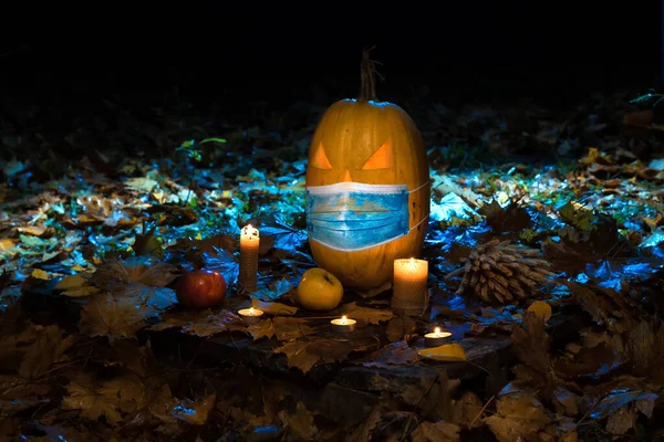 Calabaza de Halloween en máscara médica y velas en bosque oscuro. Concepto de fiesta protegida halloween durante el Covid-19 — Foto de Stock