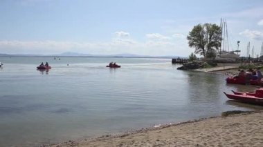 Umbria, İtalya - 14 Ağustos 2019: Sualzo sahilinde dinlenen ve Trasimeno Gölü'nde pedalos kullanan turistlerin pan çekimi